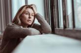 Woman looking out window holding head