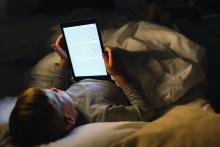 A young boy uses his e-reader in bed.