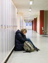 An unhappy teen sits on the floor in a hallway at school