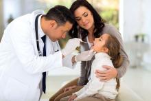 Girl sits with her mom as doctor uses tongue depressor