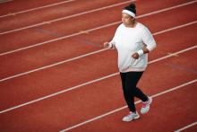 Overweight African American woman jogging on running track to lose weight