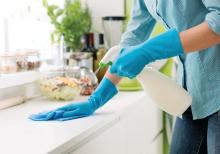 Woman cleaning a kitchen countertop with a spray detergent.