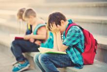 Boy with head in hands, children with rucksacks sitting on the stairs near school