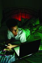 Teenager on his bed, looking at a laptop computer.