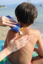 An individual applies sunscreen to a child's back