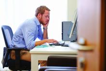 A weary man slouches over a computer