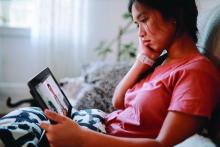 A young woman uses a digital tablet to have a telemedicine video meeting with her doctor