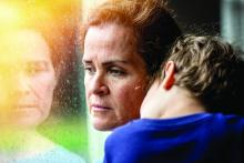 A worried woman holds a young boy while looking through a window