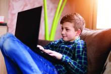 Young boy sitting on sofa and using laptop