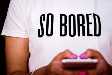 A woman texts while wearing a T-shirt that says, &quot;so bored.&quot;