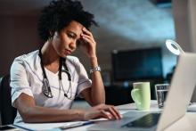 A worried doctor holds her head while working at a laptop