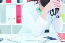 young female medical doctor sitting at the desk in office head in hands