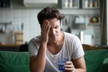 Man with headache sitting on couch drinking water