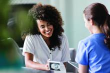 Young mixed race woman smiles while looking at her baby's ultrasound image. She is meeting with a home healthcare nurse.