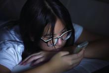 A teenager in bed looks at her mobile phone.