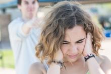Teenage girl with her hands covering her ears while her boyfriend is yelling at her